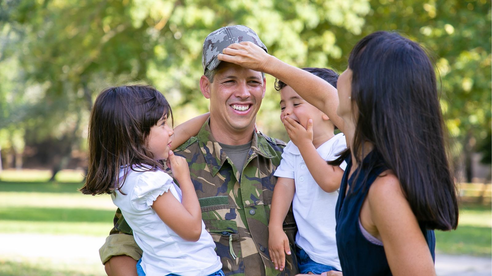 Smiling service member in uniform with his wife and two children in a sunny park