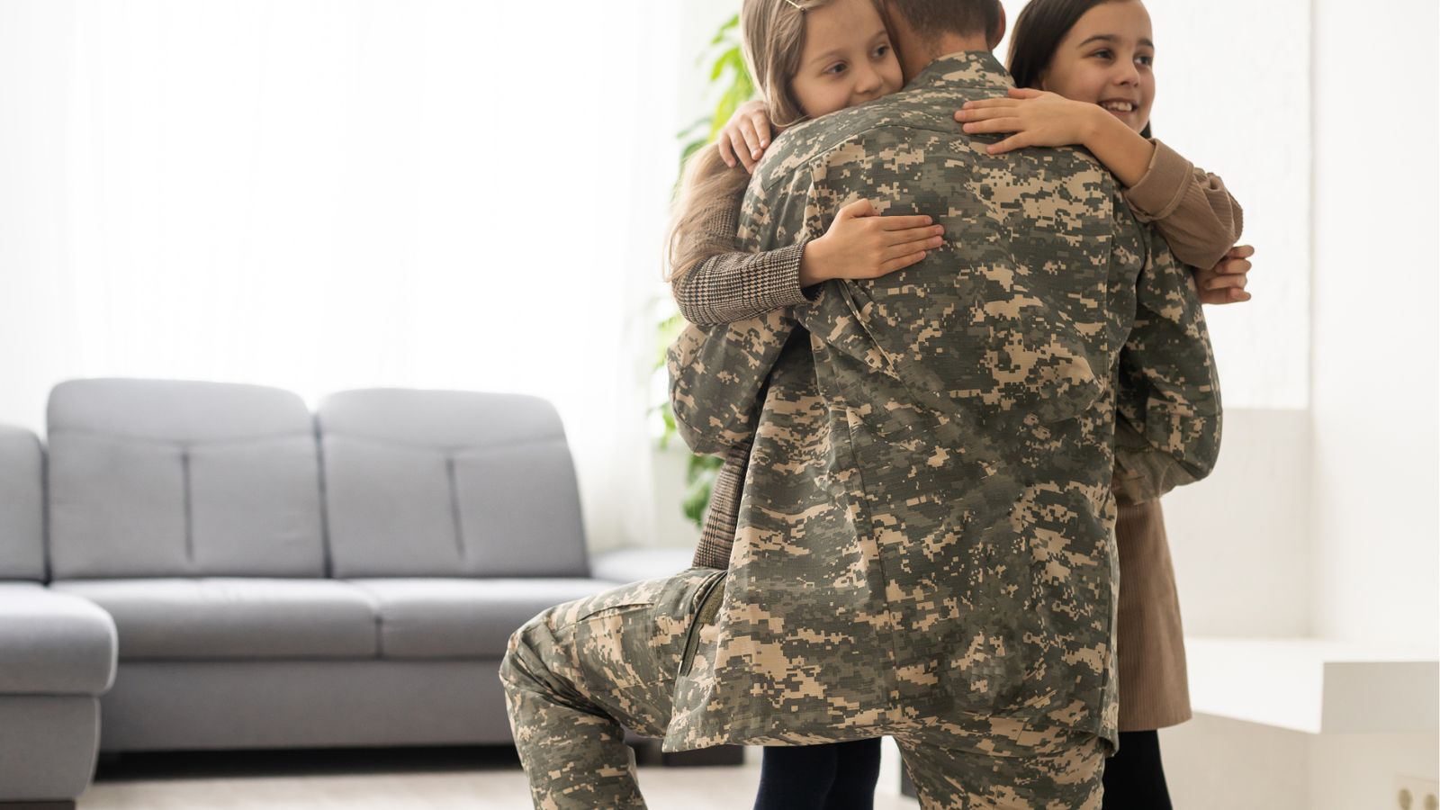Service member in uniform hugging family at home in a bright living room