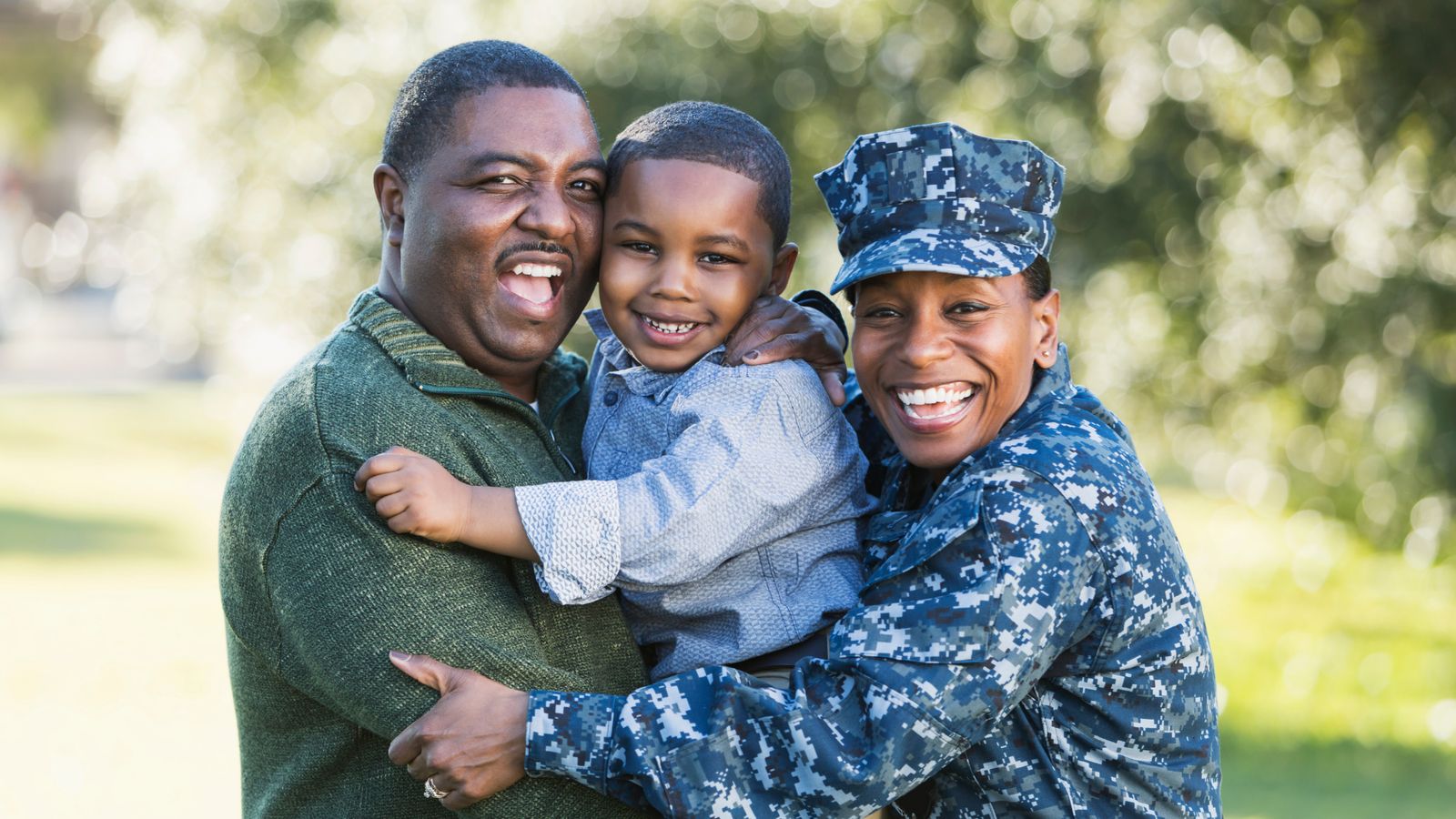 Navy service member hugging her husband and son outdoors