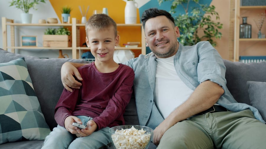 A dad and son smiling on the couch with popcorn