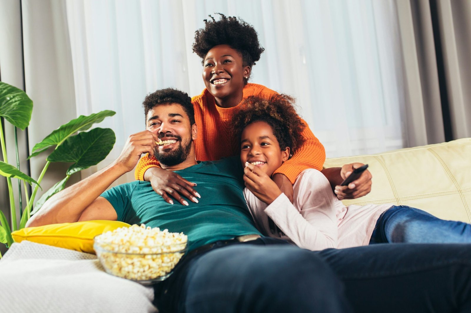 A family laughing on the couch with popcorn and the remote