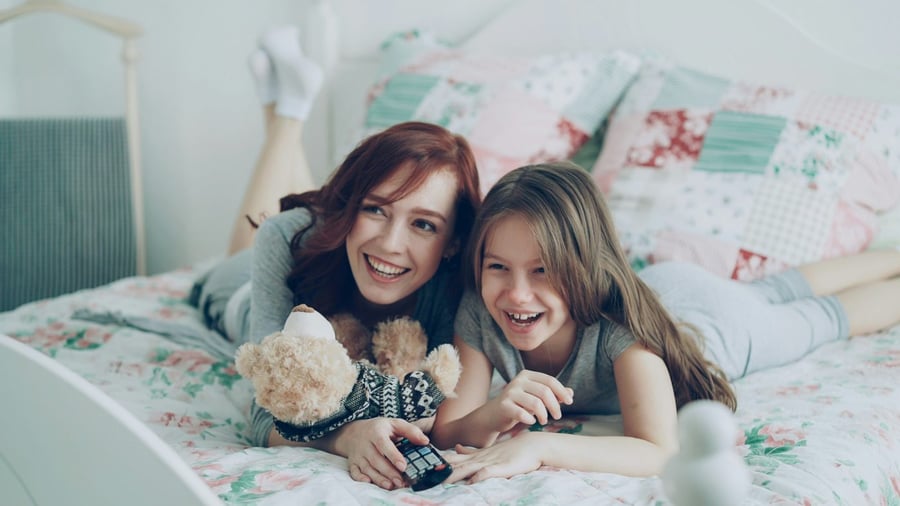 A mom and daughter laughing at a show in bed