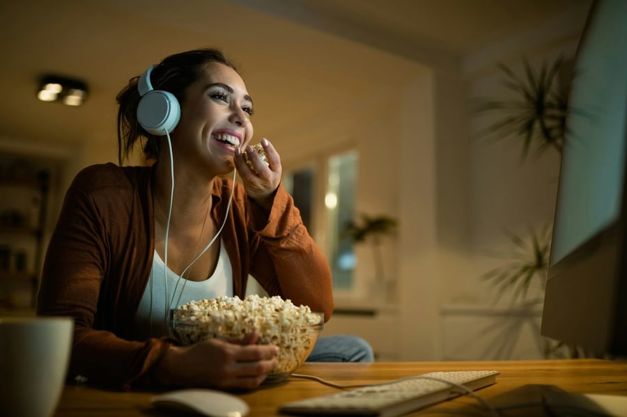 A woman laughing with headphones and popcorn at night