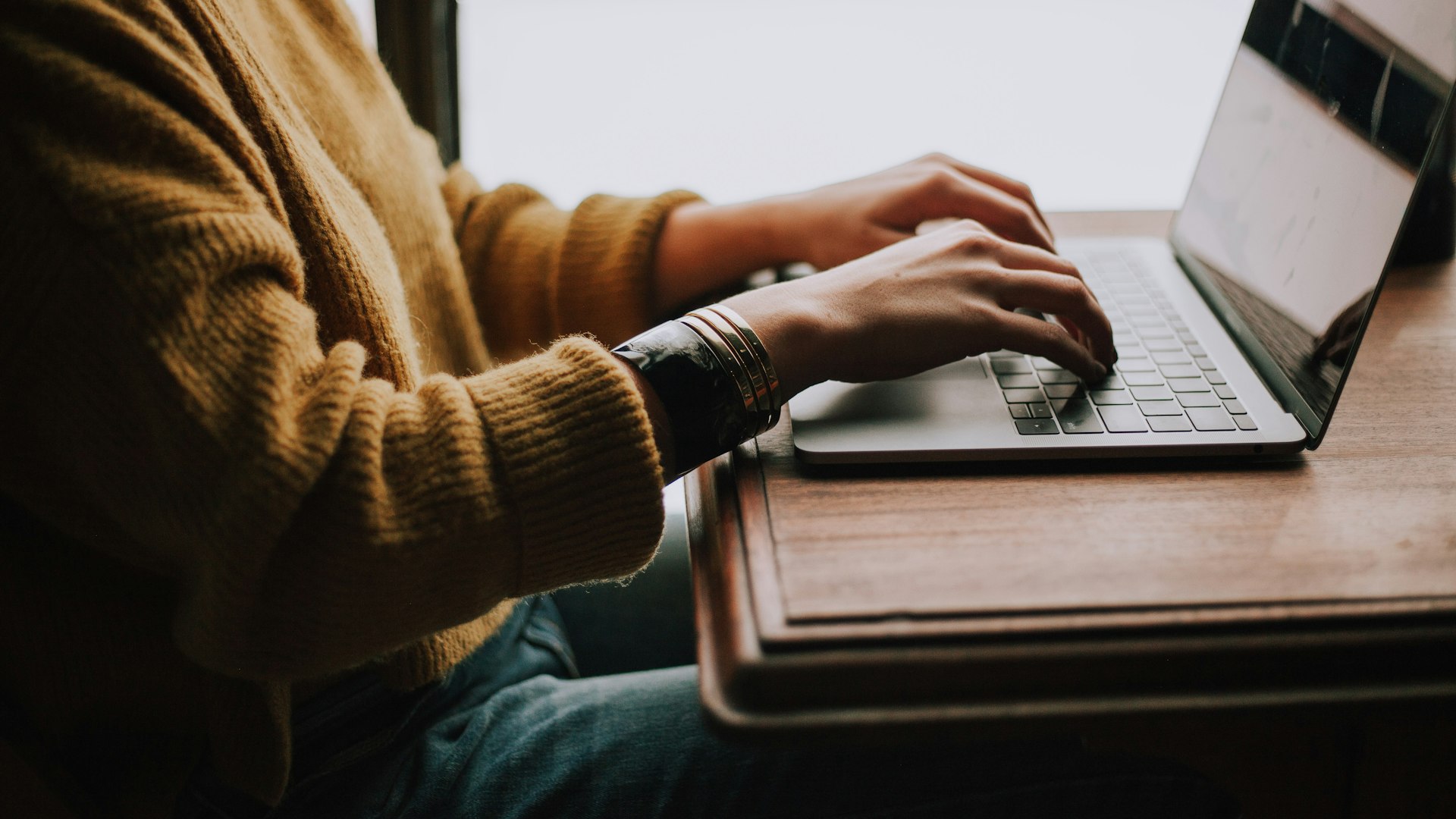 Hands typing on a laptop at a wooden desk