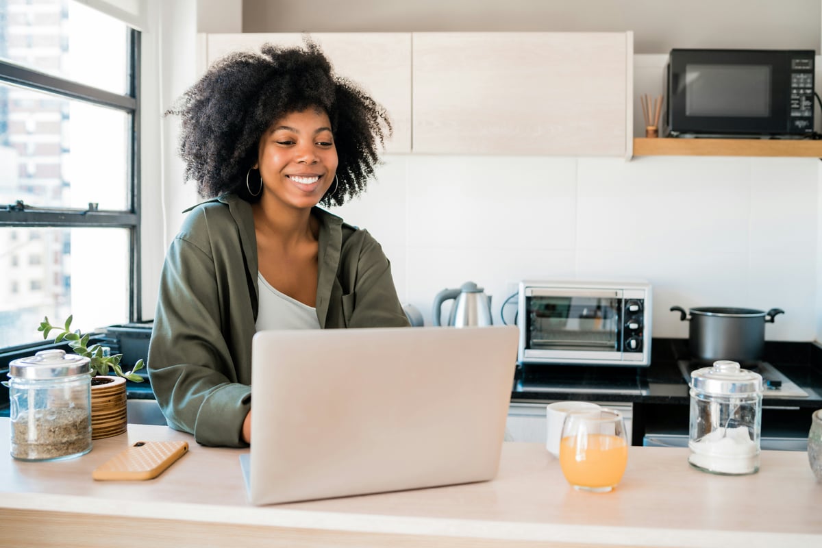Smiling woman working on a laptop at her kitchen counter