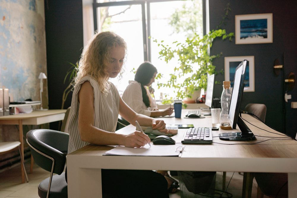 Two coworkers work at computers in a bright small office