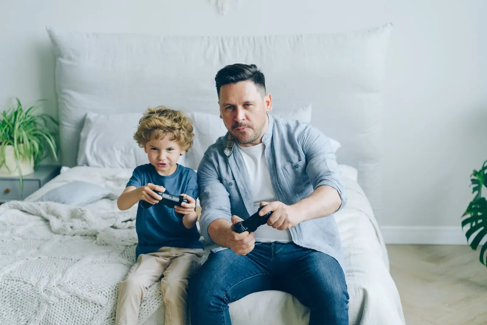Dad and son playing video games together on a bed