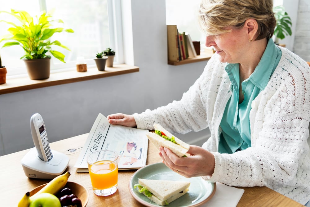 Woman reading the newspaper at her kitchen table beside a cordless home phone