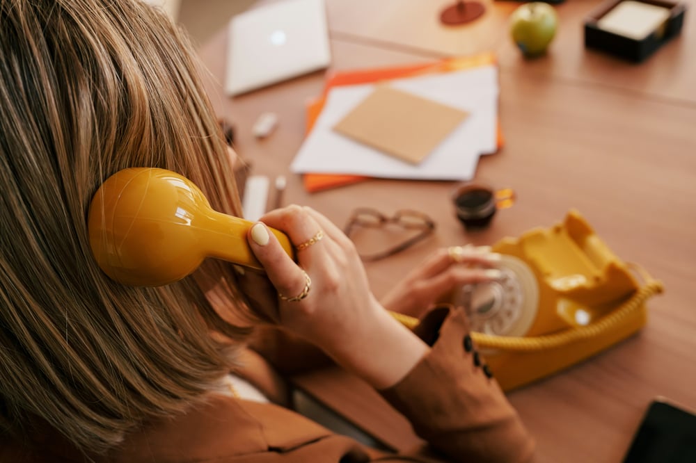 Woman dialing a yellow rotary telephone