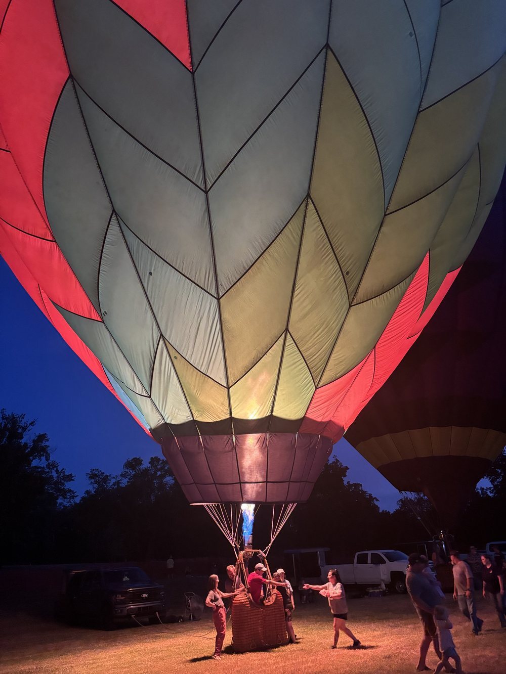 A hot air balloon glowing at dusk as families gather around the basket