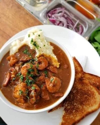 A bowl of shrimp in a dark, rich sauce with mashed potatoes, parsley and toasted bread at The Owl Shoppe